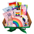 A Pride-themed gift box containing various items including a rainbow-colored bath bomb, a pride flag chocolate bar, a rainbow-coated gummy bear, a pride progress pin, a 'Love Is Love' mug, a rainbow coaster, a 'Equality Is Cool' vinyl sticker, a bookmark, a decal, and a snapback hat with a pride flag design.