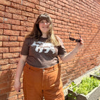 Emily stands in the sun wearing Roaming Bear t-shirt in brown.
