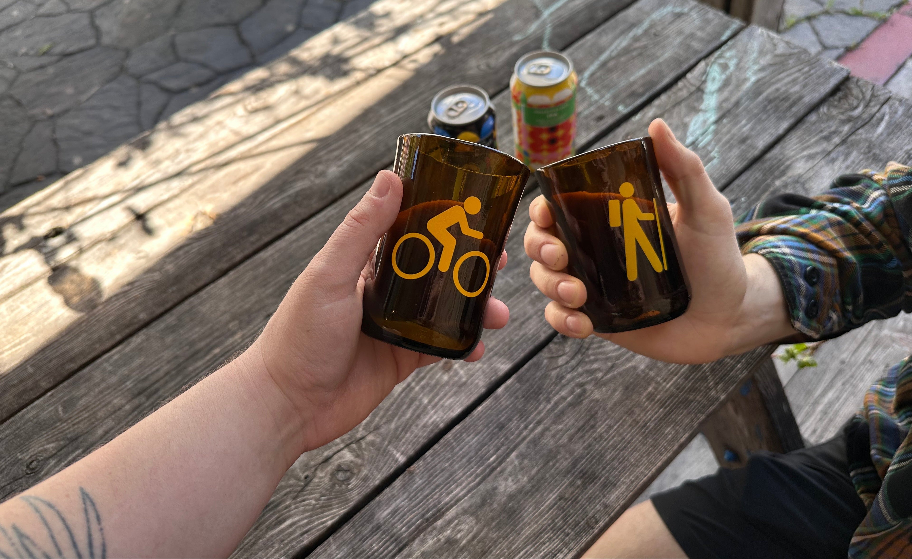 Two people holding glasses with cycling and walking symbols at a wooden table.