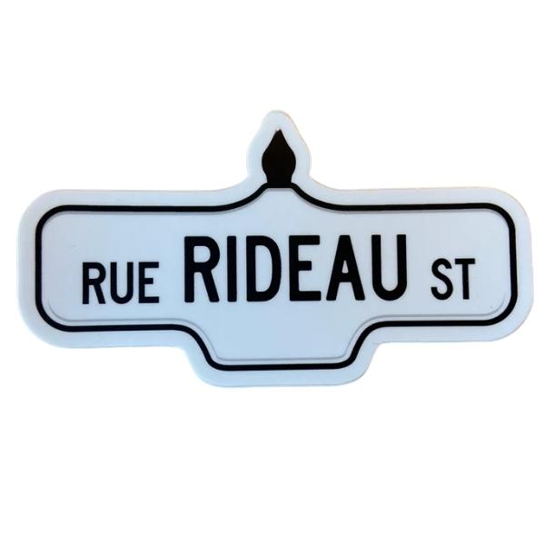 Sticker of a white street sign with black text that reads 'Rue Rideau St'.