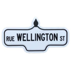 Sticker of a white street sign with black text that reads 'Rue Wellington St'.