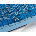 Card with blue background showing an illustration of a cozy winter A-frame cabin nestled in the trees. Snow is on the ground and falling from the sky. Silver text reads "Cozy Holiday Wishes".