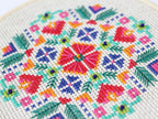 Cross stitch pattern that looks like flowers in red, orange, green, blue, and pink.  This picture is an extreme close-up.... woah.