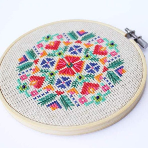 Cross stitch pattern that looks like flowers in red, orange, green, blue, and pink.